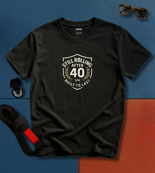 Black BJJ t-shirt with 'Still Rolling After 40 Built to Last' design on a blue and orange gradient background.